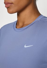 T-shirt à manches courtes Nike en tissu bleu clair avec une texture lisse. Présente un logo Nike blanc subtil sur la poitrine et un col rond.
