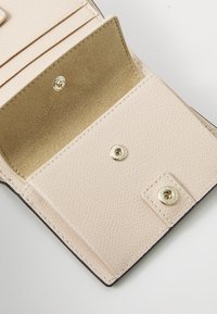 Light pink leather wallet interior with textured finish, featuring a golden snap closure and soft beige lining.