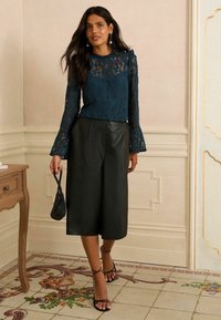 Čipkast zgornji del v temno smaragdno zeleni barvi z dolgimi, razširjenimi rokavi; v kombinaciji s črnimi usnjenimi culottes hlačami in črnimi sandali z naramnicami. Dopolnjeno z majhno torbico.