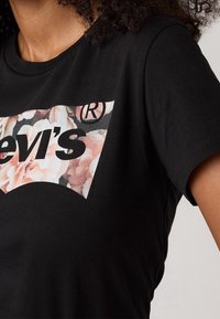 Svart bomullströja med ett blommigt grafiskt mönster i nyanser av rosa och vitt, med "Levi's"-logotypen i fet svart stil.