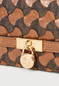 Sac en cuir marron et noir à motifs, avec textures circulaires et un détail de cadenas doré. Comprend un logo de marque visible.