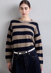 Pulover bej și bleumarin cu dungi, cu mâneci lungi, guler rotund și textură moale, asortat cu o fustă din denim închis și o curea albă.
