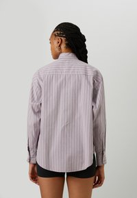 Long-sleeve shirt in light purple with vertical stripes. Features a collar and button cuffs, made from smooth fabric. Longer back hem.
