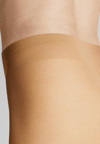Beige Oberschenkelstrümpfe mit einer glatten, transparenten Textur. Das Band oben ist elastisch und sorgt für einen engen Sitz, ohne sichtbare Linien.