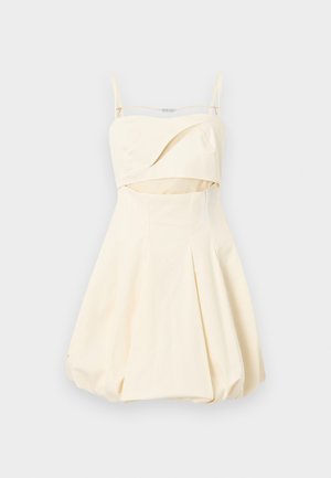 Kremasta brezramna obleka z mehurčasto krilo, tanke zlate verižice in majhen izrez pod prsmi.