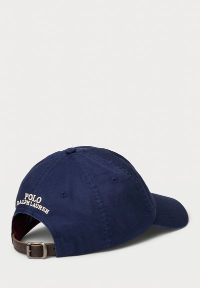 Tumši zils kokvilnas beisbola cepure ar izliekto vizieri, regulējams brūns ādas siksniņa un izšūts "Polo Ralph Lauren" logo aizmugurē.