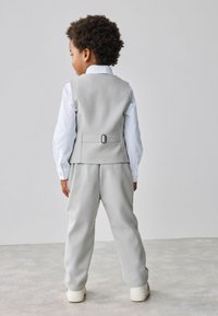 Completo grigio per bambini, composto da un gilet su misura con dettaglio della cintura, una camicia bianca a maniche lunghe e pantaloni a vestibilità comoda.