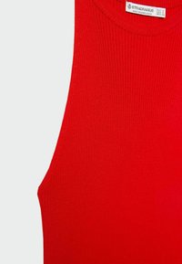 Gros plan sur un haut sans manches rouge en maille côtelée avec un col rond et une étiquette blanche indiquant la taille à l'intérieur du col.