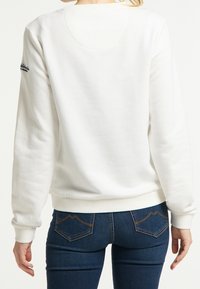 White sweatshirt with a round neck and ribbed cuffs, featuring a plain texture. Paired with blue jeans showcasing stitched pockets.