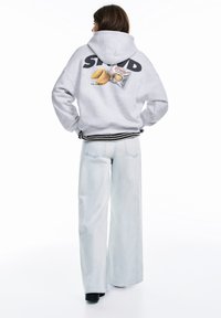 Hanorac gri deschis cu textul "STWD", având un grafic cu o prăjitură a norocului pe spate. Asortat cu blugi largi albaștri deschiși.