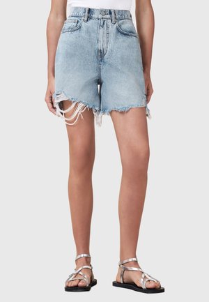 Lichtblauwe denimshorts, hoog in de taille, met rafelige zoom en versleten details, gecombineerd met platte zilveren sandaaltjes.