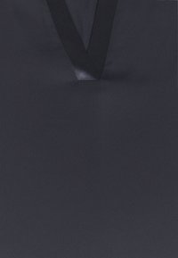 Haut noir à col en V avec une bordure lisse et légèrement brillante autour de l'encolure sur un tissu mat.