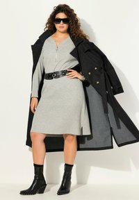 Abito grigio a coste con zip, trench coat nero con bottoni dorati, cintura nera con borchie e stivaletti neri con tacco e finitura testurizzata.