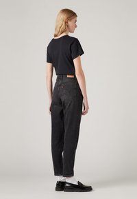 Black t-shirt and high-waisted dark gray jeans. Jeans feature back pockets and a leather tag. Model wears black loafers and white socks.