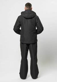 Schwarze wasserdichte Jacke mit Kapuze und elastischen Bündchen, kombiniert mit dazu passenden lockeren Hosen. Glatte Textur, entworfen für den Outdoor-Einsatz.