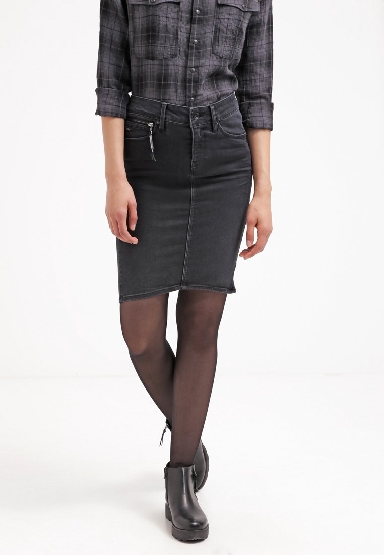 Svart denimkjol med smal passform, med dragkedja framtill, slät textur och rå kant. Kombinerad med svarta ankelskor och genomskinliga strumpbyxor.