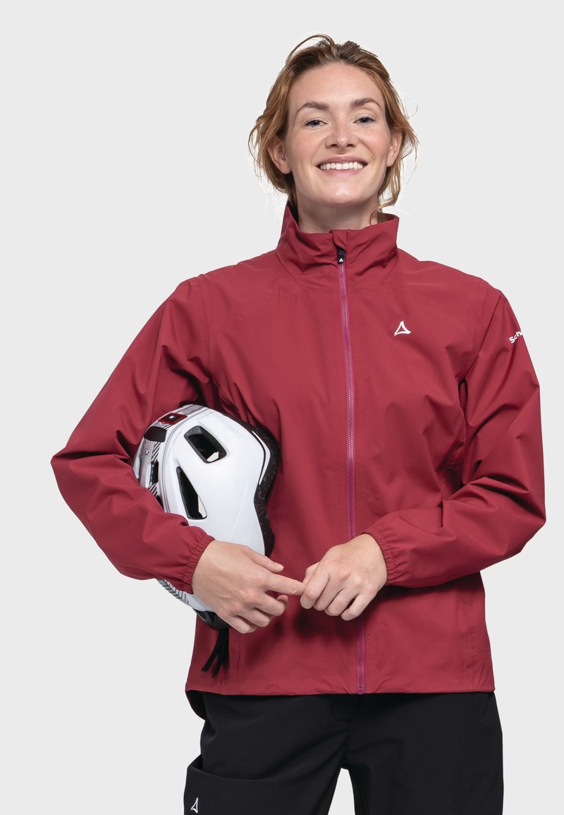 Rote wasserdichte Jacke mit hohem Kragen, Frontreißverschluss und elastischen Bündchen. Das Modell hält einen weißen Helm und zeigt ein schlankes, modernes Design.