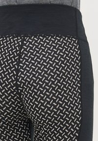 Fekete sport leggings, amelyek textúrázott derékrésszel és fehér zig-zag mintázattal díszítetták a lábakat. Puha, rugalmas anyag.