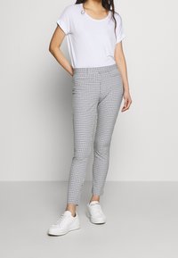 Grafitowe spodnie w kratkę o slim fit, z dwiema przednimi kieszeniami i elastycznym pasem, zestawione z białą koszulką z okrągłym dekoltem i białymi sneakersami.