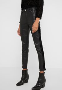 Zwarte leren broek met een strakke pasvorm, voorzien van zilveren knopen en een contrasterende zwarte velours zijstreep, gecombineerd met enkellaarzen.