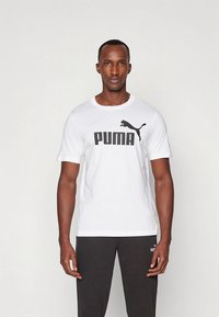 Witte T-shirt met korte mouwen, voorzien van een groot zwart Puma-logo op de borst, gecombineerd met donkergrijze sportbroek.