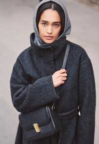 Dark gray wool coat with a high collar and wide sleeves, paired with a gray hood. Black leather bag with a gold clasp detail.