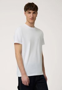 Witte katoenen t-shirt met een ronde hals, korte mouwen en een eenvoudig ontwerp. Heeft een klein logo op de linkerborst. Draagt met donkere spijkerbroeken.