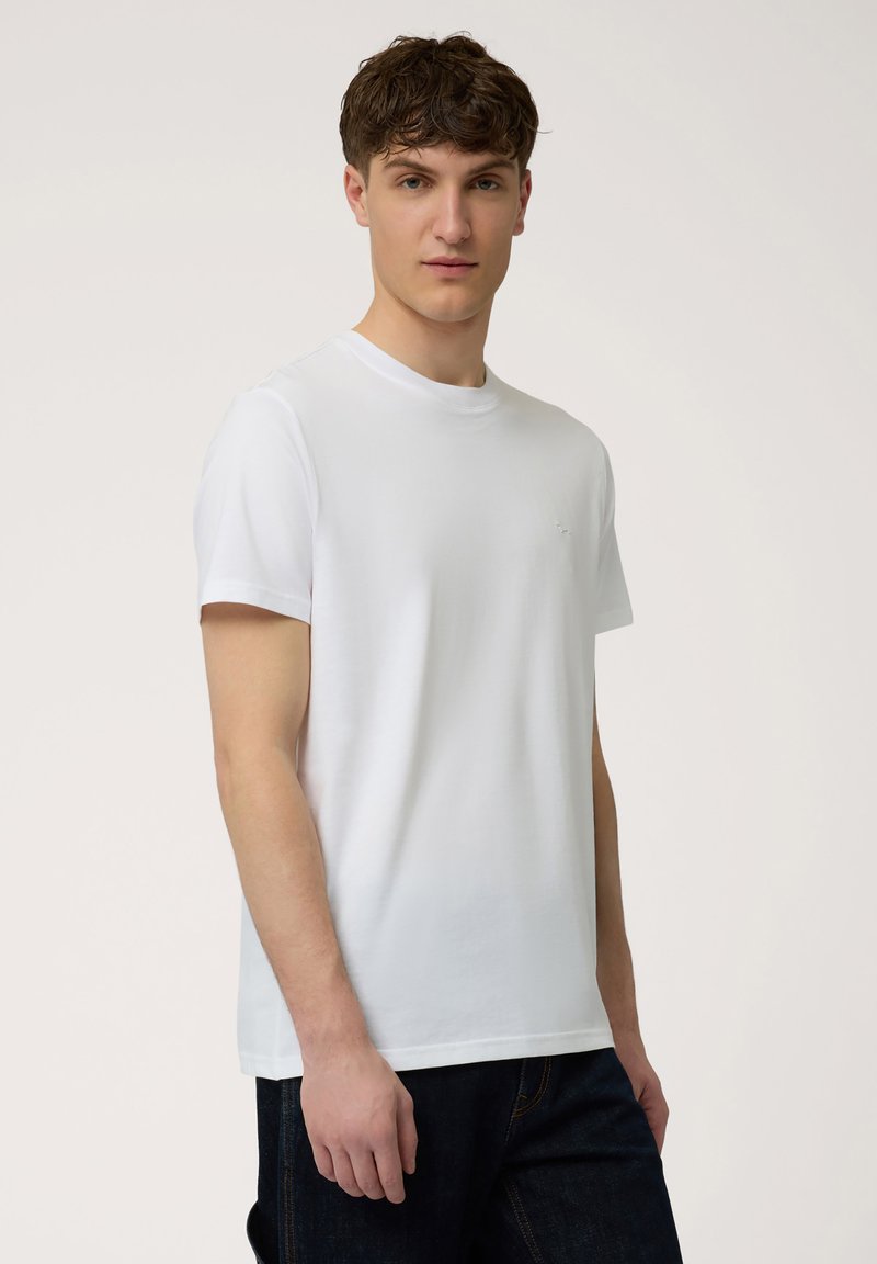 Witte katoenen t-shirt met een ronde hals, korte mouwen en een eenvoudig ontwerp. Heeft een klein logo op de linkerborst. Draagt met donkere spijkerbroeken.
