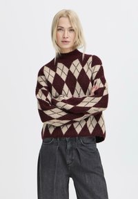 Maglione a maglia con un motivo argyle bordeaux e beige, collo alto, vestibilità ampia e polsini a coste. Abbinato a jeans grigio scuro.
