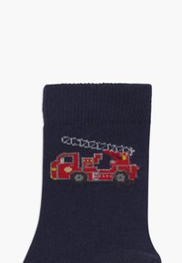 Chaussettes bleu marine ornées d'un motif coloré de camion de pompiers rouge avec des détails argentés et des roues noires, fabriquées en tissu doux au toucher.
