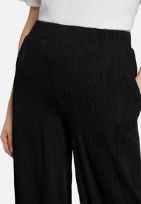 Black wide-leg pants featuring a textured wave pattern, with a stretchy ribbed waistband and side pockets, capturing a sleek design.