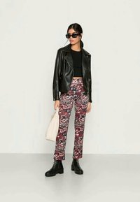 Jaqueta de motociclista de couro preta, top cropped preto justo, calças com padrão marmoreado multicolorido, botins pretos e mala tote bege.