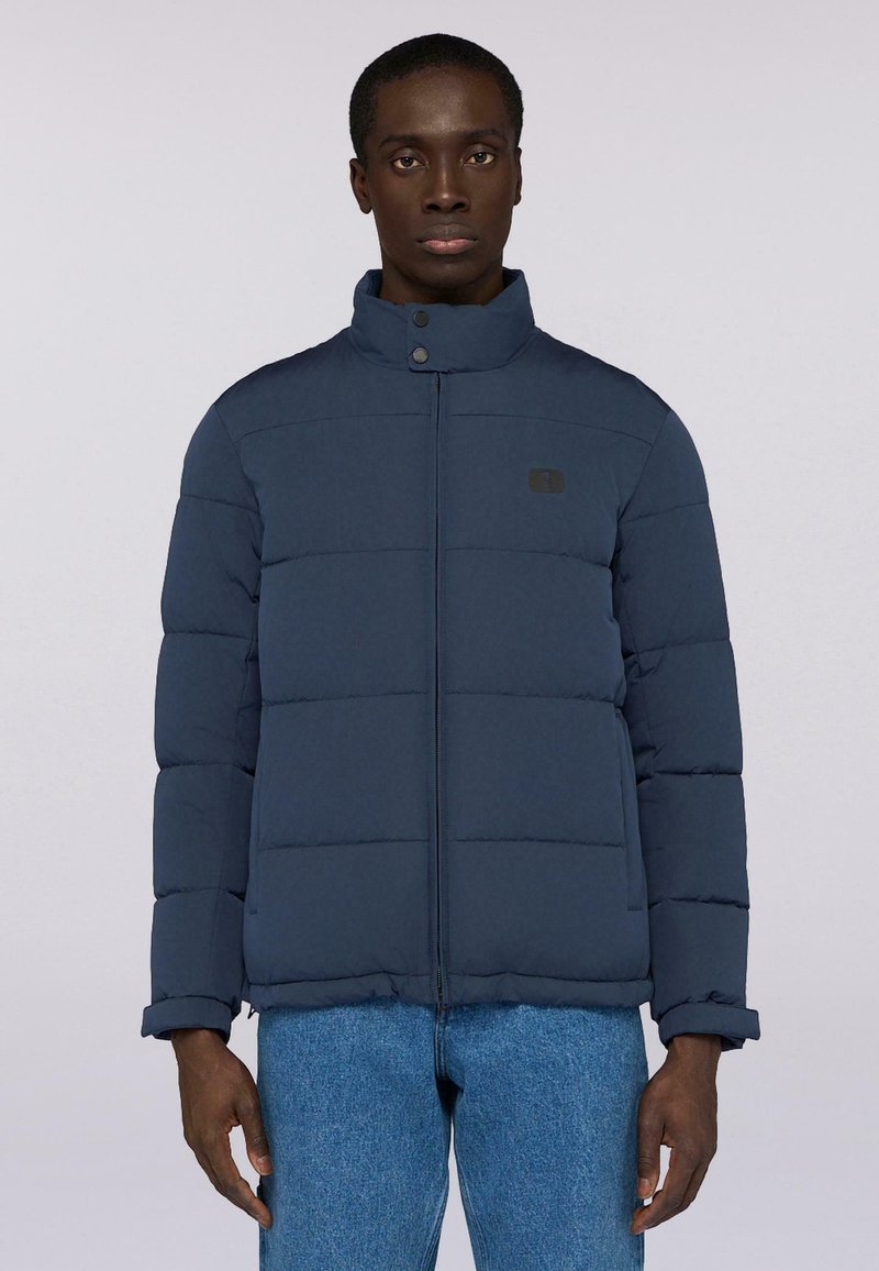 Giacca a vento trapuntata blu navy con colletto alto, chiusura con zip e un piccolo logo sul petto. Texture morbida e design imbottito per il calore.
