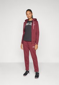 Sudadera burdeos, pantalones a juego, camiseta gris con letras blancas y zapatillas deportivas negras. Tejido suave, diseño con cremallera y acentos de logotipo.