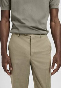 Beige skräddarsydda byxor med rak passform, med platt framsida, bältesöglor och sidofickor, i kombination med en åtsittande olivgrön pikétröja.