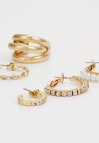 Uma coleção de brincos dourados com diversos designs: torcidos, lisos, com pérolas e outros decorados com pedras transparentes.