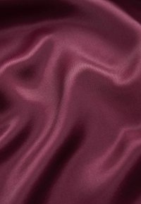 Burgundska satenasta tkanina s glatkom, sjajnom teksturom, koja sadrži blage valove i nabore. Površina odražava svjetlost, ističući njezinu bogatu boju.
