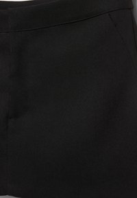 Primo piano di un tessuto nero con una trama a diagonale e cuciture visibili lungo la vita e la cucitura laterale.