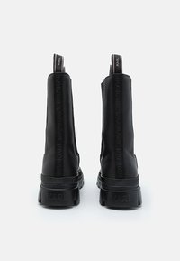 Bottes noires de cheville avec une finition en cuir lisse, des panneaux latéraux élastiques et une semelle en plateforme texturée avec un marquage contrastant à l'arrière.
