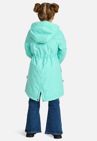 Šviesiai turkio spalvos striukė su kapišonu, raišteliu juosmenyje ir atspindinčiais akcentais. Ypatybės: ilgas, tiesus kirpimas ir skilimas nugaroje, leidžiantis judėti.