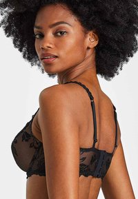Soutien-gorge en dentelle noire avec broderie florale, bretelles ajustables et fermeture à crochet et œillet. Matériau transparent avec des détails complexes.