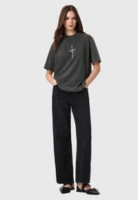Kullsort oversized t-shirt med et centralt logo, parret med højtaljede sorte wide-leg jeans og sorte slip-on sko. Enkel design.