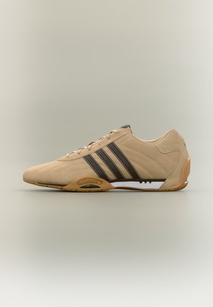 Zapatilla deportiva beige con tres rayas marrón oscuro, parte superior de ante, diseño texturizado, suela de goma y soporte acolchado para el tobillo.