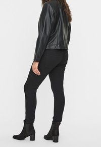 Veste en similicuir noir à coupe classique, associée à un jean skinny noir. Comprend des bottines noires à talons blocs avec une texture douce.