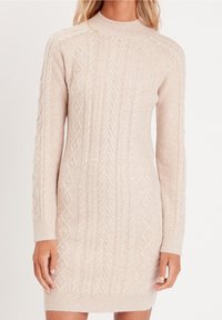 Robe-pull en maille beige clair, dotée d'un col montant et de motifs torsadés complexes sur toute la surface. Manches longues avec poignets et ourlet côtelés.