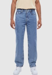 Light blue denim jeans with a straight-leg cut, five-pocket design, and visible stitching. Paired with white sneakers.