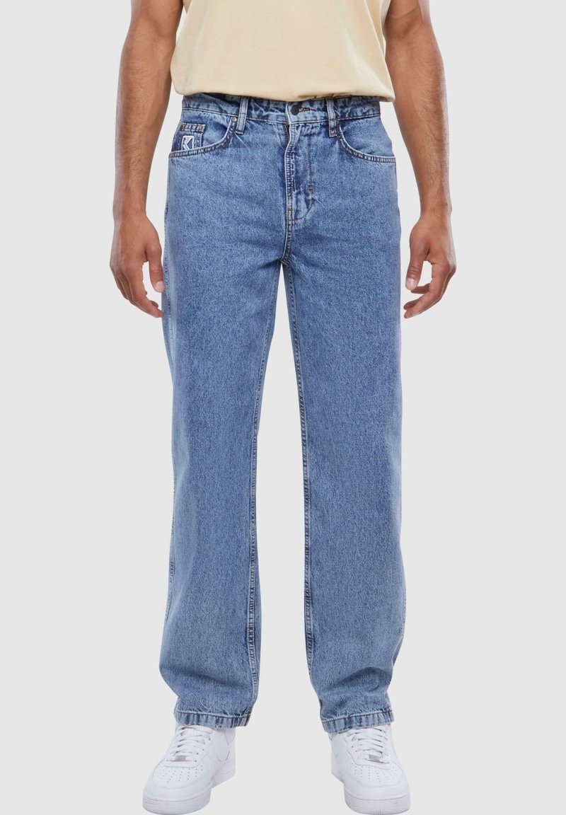 Light blue denim jeans with a straight-leg cut, five-pocket design, and visible stitching. Paired with white sneakers.