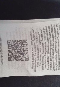 Bijela tkanina oznaka s QR kodom, otisnuti tekst na više jezika o podrijetlu i uputama za njegu, blago naborana tekstura.