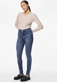 Stripet langermet topp i beige og hvitt, kombinert med høyhælte blå jeans. Modellen har på seg svarte loafers med tykk såle.