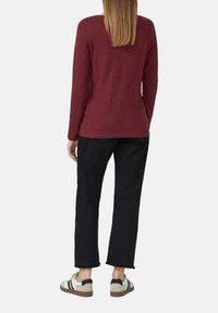 Bordeaux rotes Langarmoberteil mit lockerem Schnitt. Kombiniert mit schwarzen, cropped Hosen und beigen Sneakern mit schwarzen Akzenten und weißen Streifen.